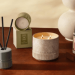 Bath & Body Works Reserve Collection products styled on a wooden table, including a lit three-wick candle, a reed diffuser, a boxed Sea Salt + Musk candle and a Vanilla + Tonka room mist.